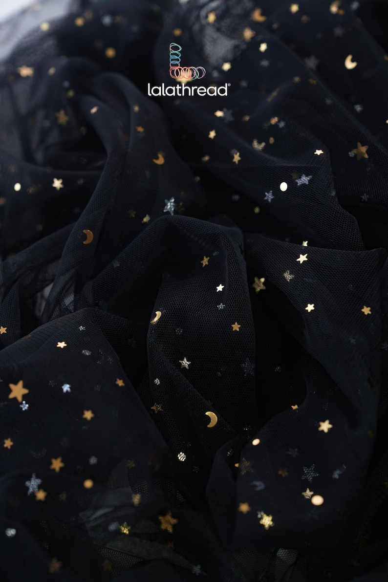 May include: Black tulle fabric with gold and silver star and crescent moon embellishments. The fabric is gathered and draped, creating a textured effect. The brand name "lalathread" is visible in the upper right corner.