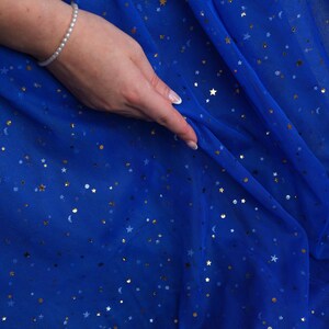 May include: Royal blue fabric with gold stars and crescent moons. The fabric is draped, with a hand wearing a pearl bracelet touching the material. The logo "lalathread" is visible in the upper right corner.