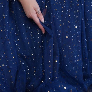 May include: A deep navy blue tulle fabric is adorned with gold stars and crescent moons. The fabric is being held by a hand wearing a silver ring and a pearl bracelet. The brand name "lalathread" is visible in the bottom right corner.