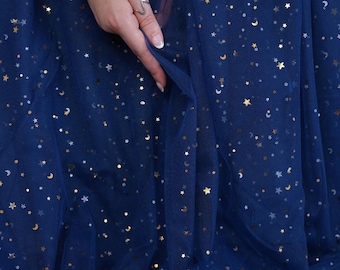 Puede incluir: Tela de tul azul marino oscuro adornada con estrellas doradas y lunas crecientes. La tela está sostenida por una mano que lleva un anillo plateado y una pulsera de perlas. El nombre de la marca "lalathread" es visible en la esquina inferior derecha.