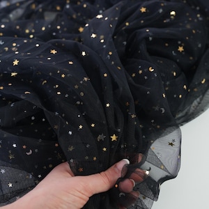 May include: Black tulle fabric with gold star and moon sequins. The fabric is gathered in the hand, showing its texture and drape. The brand name "lalathread" is visible in the upper left corner.