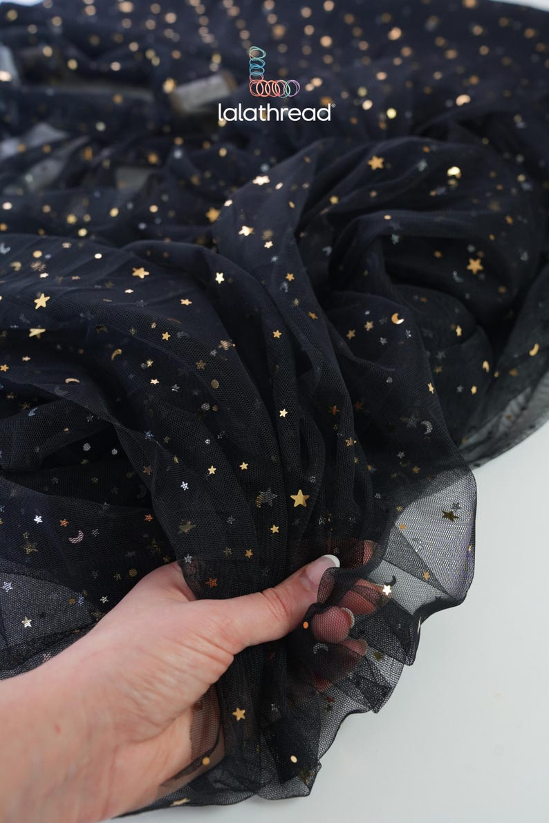 May include: Black tulle fabric with gold star and moon sequins. The fabric is gathered in the hand, showing its texture and drape. The brand name "lalathread" is visible in the upper left corner.