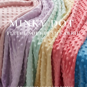 May include: A selection of soft, plush Minky Dot fleece fabric in pastel shades. The fabric is 152 cm wide and has a dotted texture. Text on the image reads "MINKY DOT FLEECE SOFT PUSH FABRIC" and "BABY BLANKETS | TOYS | QUILTING | PILLOW COVERS."