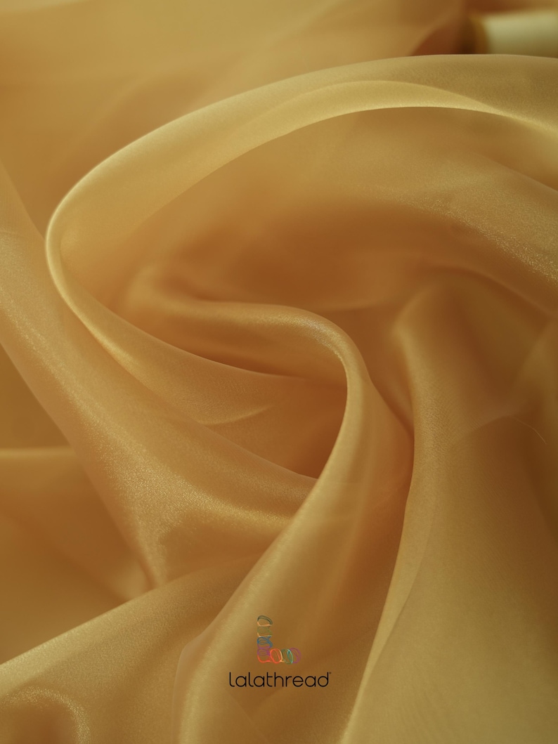 May include: A close-up of a sheer, golden yellow fabric. The fabric is draped and folded, showing its texture and transparency.