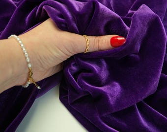 May include: Close-up of a luxurious, deep purple velvet fabric. The fabric is draped and held by a hand wearing a gold ring and a pearl bracelet. The brand name "lalathread" is visible in the upper right corner.