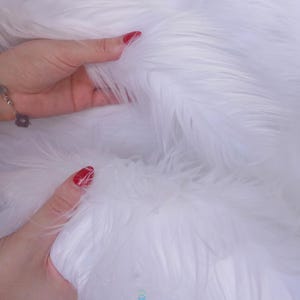 May include: A plush white faux fur fabric with long, soft fibers. The material has a dense, shaggy texture and a bright, clean white color throughout. The brand name lalathread is printed in small, lowercase letters at the bottom center.