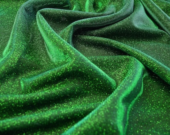 May include: Close-up of a shimmering green fabric with a textured surface. The fabric is draped, creating folds and shadows that highlight its glittery appearance. The material has a subtle sheen, reflecting light and adding depth to the overall look. The fabric is likely used for apparel or decorative purposes.