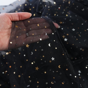 May include: Black tulle fabric with gold and silver star and crescent moon embellishments. The fabric is semi-sheer, with the brand name "lalathread" visible in the background. This fabric is suitable for apparel and craft projects.