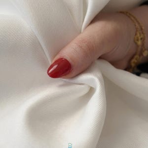 May include: A thumb with a glossy red fingernail rests against a piece of white fabric with a visible diagonal twill weave. At the bottom center, a small logo features the text lalathread in white letters below a stylized letter L icon.