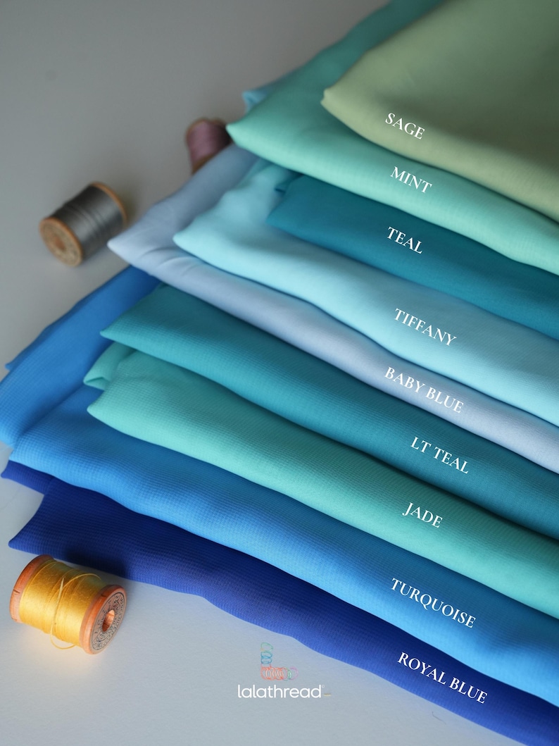 K&ouml;nnte beinhalten: Stoffmuster in verschiedenen Blau- und Gr&uuml;nt&ouml;nen, von Salbei bis K&ouml;nigsblau. Die Farben sind beschriftet, mit sichtbaren Garnrollen. Das Bild zeigt eine Auswahl an Textilfarben.