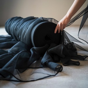 May include: A roll of black sheer fabric is being held by a hand. The fabric is soft and flowing, and it has a delicate texture.