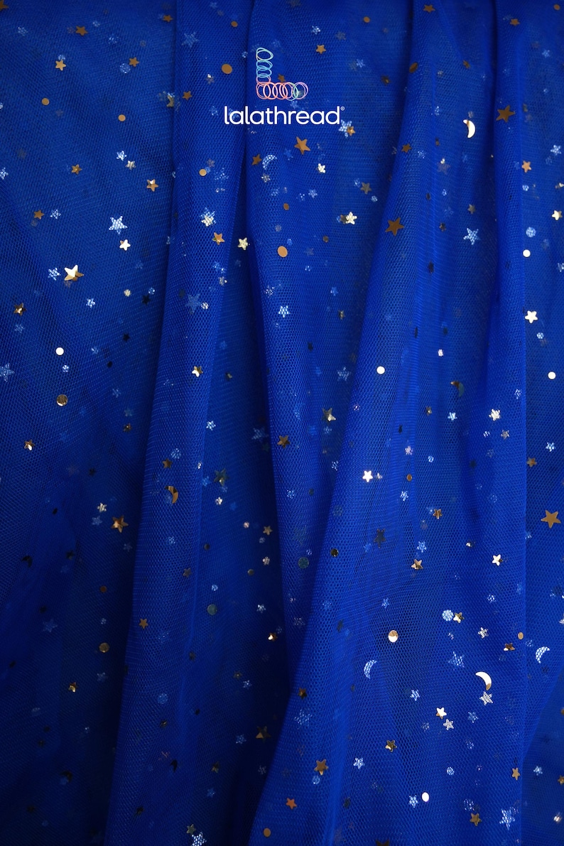 May include: Royal blue tulle fabric with gold star and dot embellishments. The fabric is draped, creating soft folds. The text "lalathread" is visible in the upper right corner. This fabric is suitable for crafting and apparel.
