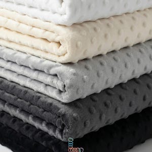 May include: Five folded blankets in a stack, ranging in colour from white to black. Each blanket has a textured, dotted pattern. The brand name "lalathread" is visible at the bottom.