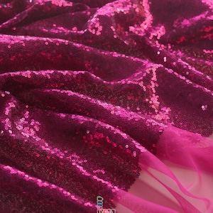 May include: Close-up of a vibrant fuchsia fabric covered in sequins. The fabric is draped, creating folds and shadows that highlight the texture and sparkle. The bottom right corner features a sheer, flowing edge. The text "lalathread" is visible.