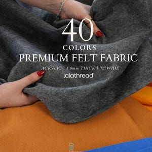 May include: A dark gray felt fabric with text that reads 40 COLORS PREMIUM FELT FABRIC ACRYLIC | 1.6mm THICK | 72"WIDE lalathread. The fabric has a soft, matte texture and is displayed alongside orange and blue felt fabric pieces.