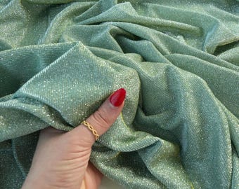May include: A close-up of a shimmering, sage green fabric with a metallic sheen. The fabric is draped in soft folds, catching the light and creating highlights. The fabric has a subtle texture and a luxurious appearance, suitable for apparel or decorative projects.