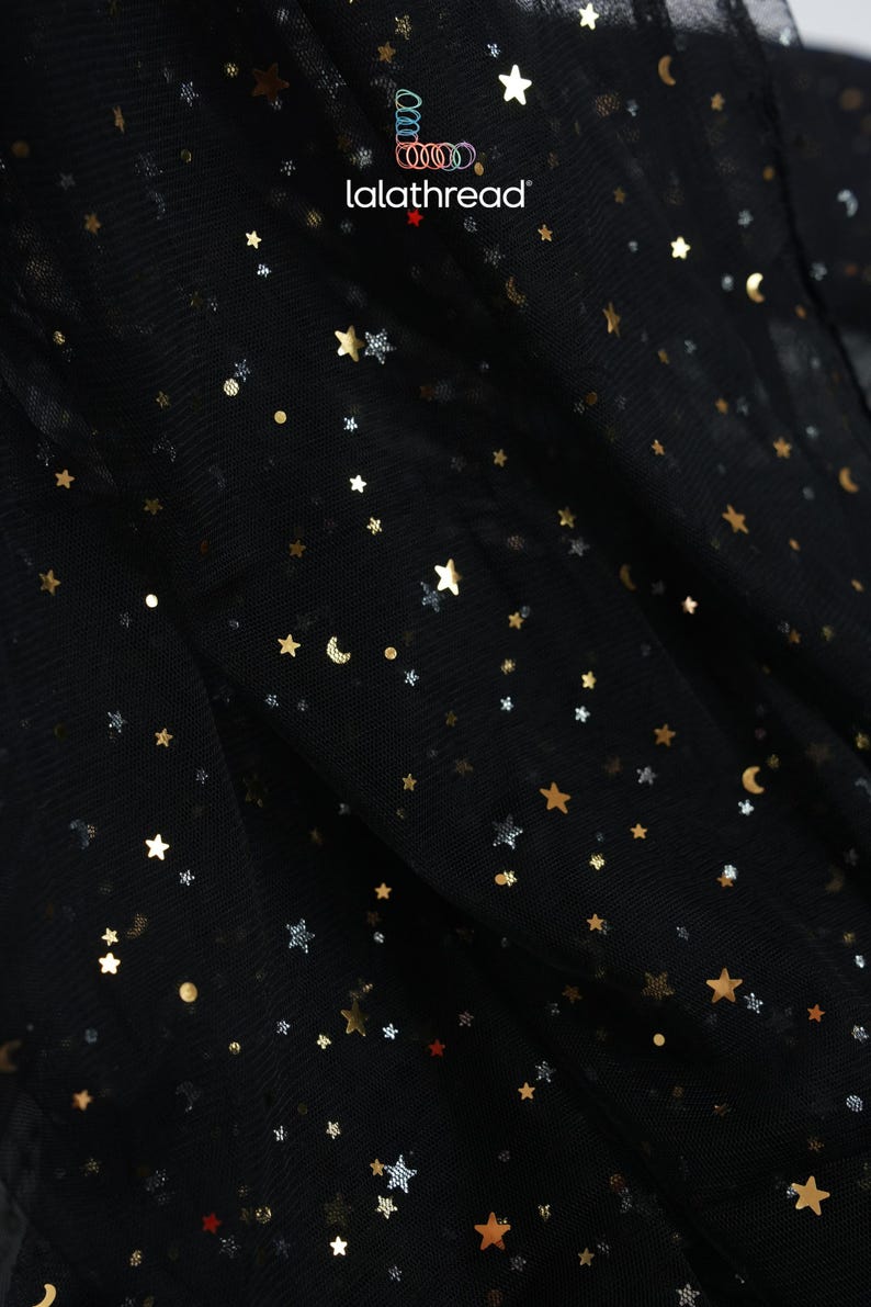 May include: Black fabric with gold and silver star and moon embellishments. The fabric has a sheer, layered appearance. The brand name "lalathread" is visible in the upper center. The overall theme is celestial.