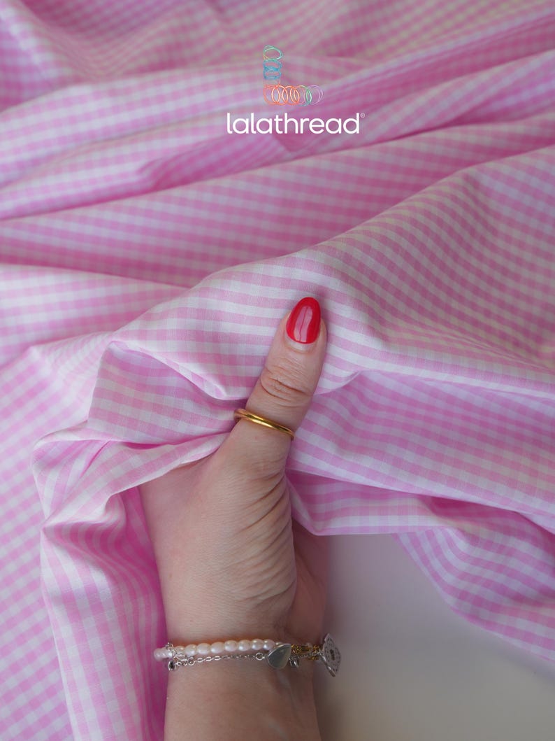 Puede incluir: Tela de cuadros vichy rosa y blanco con el texto "lalathread". La tela est&aacute; sujeta por una mano con un anillo dorado y una pulsera. El esmalte de u&ntilde;as es rojo.