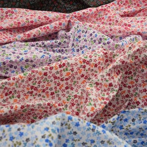 May include: A collection of folded fabric pieces featuring a repeating small floral print in various colorways including black, pink, white, and blue. The fabric displays a dense pattern of tiny blossoms and leaves. The text lalathread is visible.