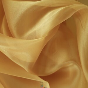 May include: A close-up of a soft, sheer, gold fabric. The fabric is draped and folded, showing its texture and drape.