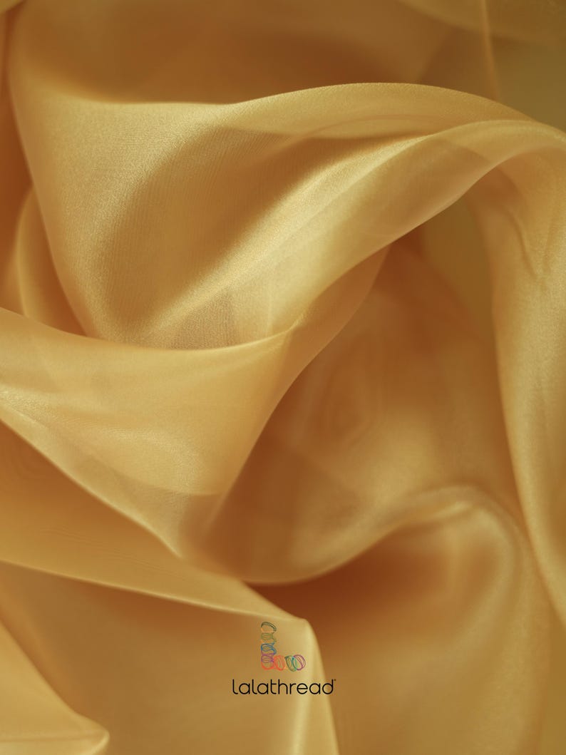 May include: A close-up of a soft, sheer, gold fabric. The fabric is draped and folded, showing its texture and drape.