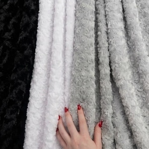 May include: A collection of plush fabric swatches featuring a raised, swirling rose pattern. The fabric is displayed in four distinct color variations, arranged side-by-side in a vertical orientation, including black, white, light gray, and dark gray.
