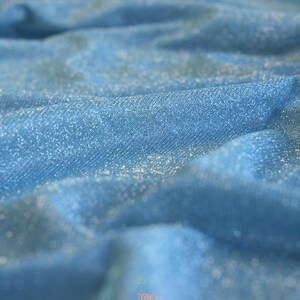 May include: Close-up of a light blue fabric with a shimmering, glittery texture. The fabric is draped, creating soft folds and shadows. The word "lalathread" is visible in the bottom right corner.