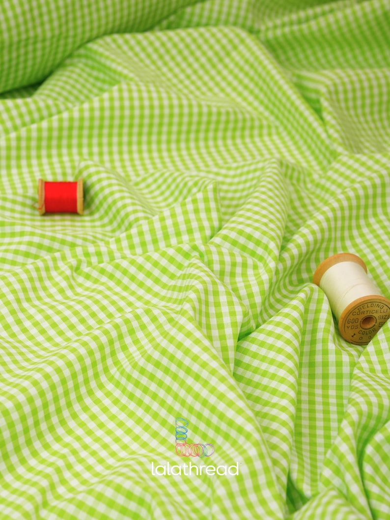 May include: Bright green and white gingham fabric with a wavy texture. Two spools of thread, one red and one cream-colored, are placed on the fabric. The fabric has the text "lalathread" in the bottom right corner.