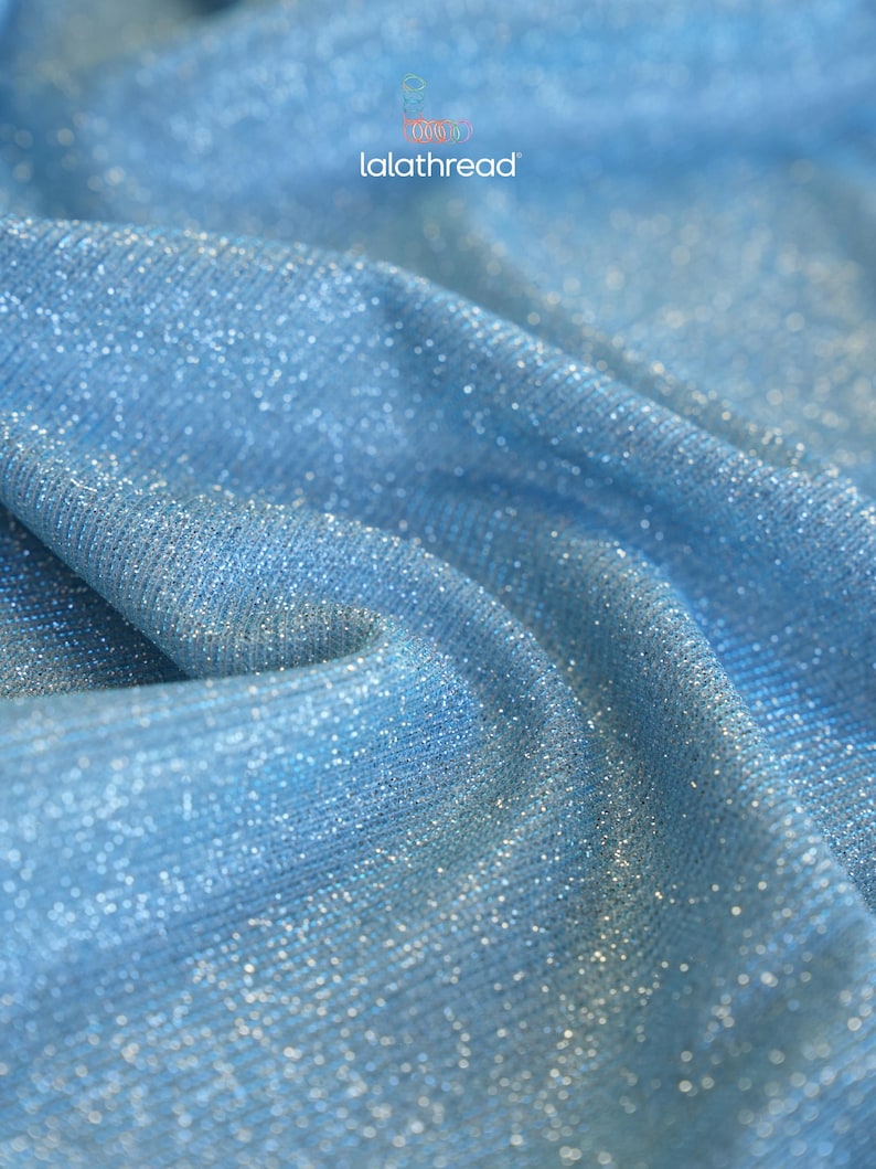 May include: Close-up of a light blue fabric with a shimmering, glittery texture. The fabric is draped, creating soft folds and shadows. The text "lalathread" is visible in the upper left corner.