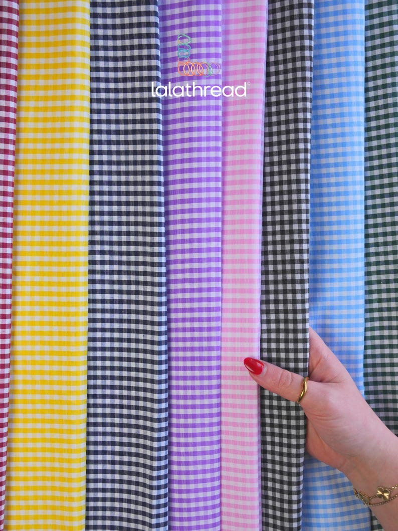 May include: A variety of gingham fabric in multiple colors, including yellow, black, purple, pink, blue, and green. The fabric is arranged vertically, with a hand holding the black and white checkered fabric. The text "lalathread" is visible.