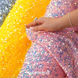 May include: Rolls of iridescent sequin velvet fabric in pink, yellow, and gray. The pink fabric is held by a hand. The text on the image reads "lalathread" and "Iridescent Sequin Velvet Fabric". The fabric is 58 inches wide.
