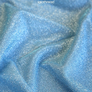 May include: Close-up of a shimmering, light blue fabric with a textured surface. The material has a subtle sparkle, catching the light and creating a luminous effect. The fabric is likely used for apparel or decorative purposes.