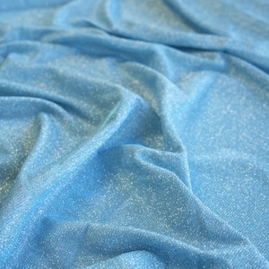 May include: Close-up of a light blue fabric with a subtle sparkle. The material is draped, creating soft folds and shadows. The fabric has a shimmering quality, suggesting it might be used for apparel or decorative purposes.