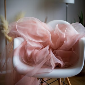May include: A soft, blush-colored tulle fabric draped over a white chair. The tulle is gathered and flowing, creating a delicate and romantic look.
