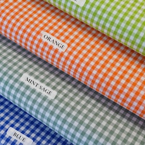 May include: Close-up of four fabric swatches in lime green, orange, mint sage, and blue gingham patterns. Each swatch has a label with its color name. The fabric is folded, showing the texture and color variations.