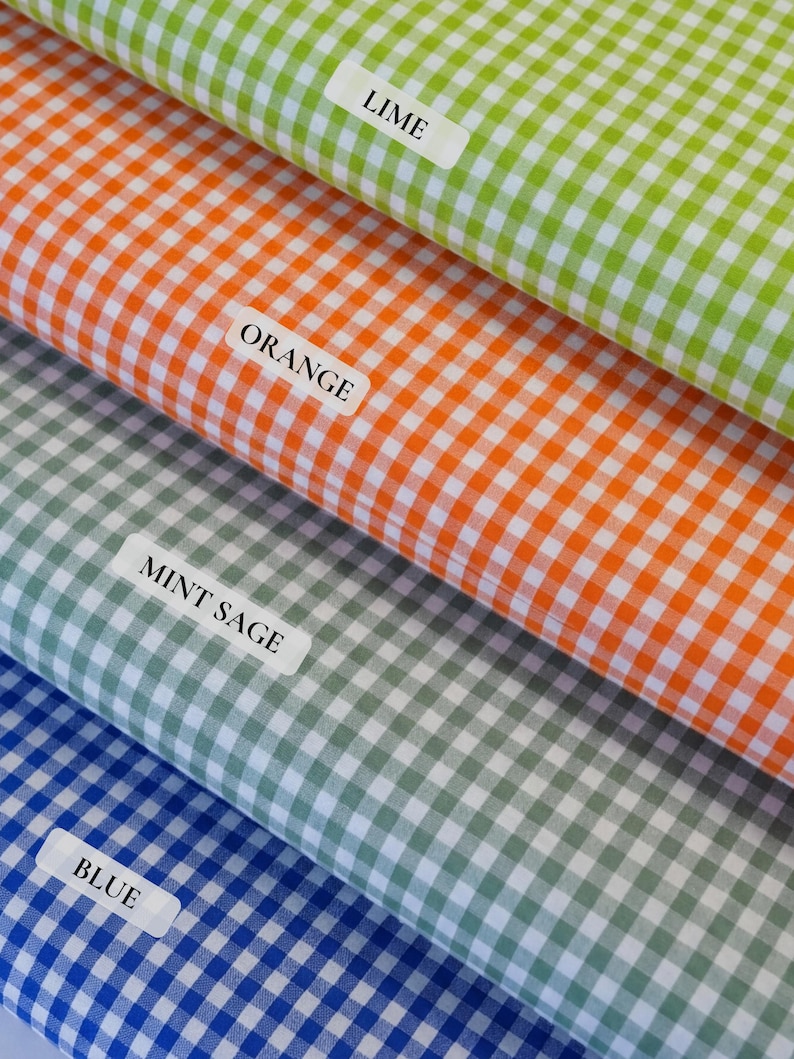 May include: Close-up of four fabric swatches in lime green, orange, mint sage, and blue gingham patterns. Each swatch has a label with its color name. The fabric is folded, showing the texture and color variations.