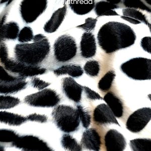 May include: Close-up of a white fabric with large, irregular black spots, resembling a Dalmatian dog's coat. The fabric has a soft, textured appearance. The logo "lalathread" is visible in the upper right corner.