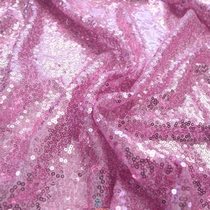 May include: Pink sequin fabric with a shimmering effect. The fabric is densely covered in small, round sequins, creating a reflective surface. The material is draped, showing folds and shadows. The word "lalathread" is visible in the bottom right corner.
