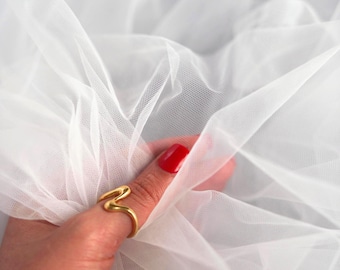 May include: A close-up of white tulle fabric, with a hand wearing a gold ring. The ring has a unique, curved design. The hand has red nail polish. The logo "lalathread" is visible in the upper right corner.