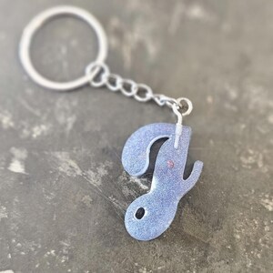 May include: A silver keychain with a sparkly silver letter J charm. The letter J is in a cursive font.