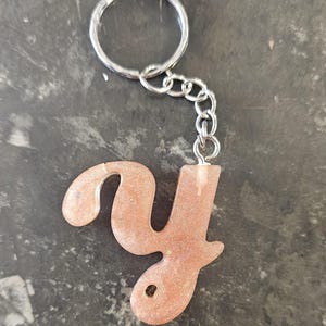 May include: A sparkly pink and gold letter Y keychain. The letter is attached to a silver key ring and chain.