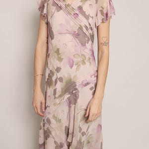 K&ouml;nnte beinhalten: Ein rosa-violettes Kleid mit floralem Muster, V-Ausschnitt und kurzen &Auml;rmeln. Das Kleid hat einen flie&szlig;enden, asymmetrischen Saum.