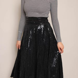 May include: A black sequin midi skirt paired with a black and white striped long-sleeve turtleneck. The skirt has a high waist and a flared silhouette. The top is a classic striped pattern.