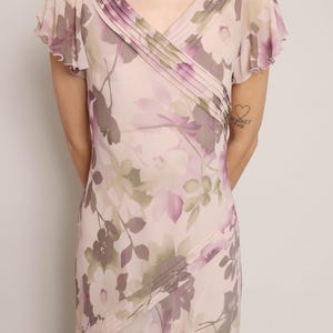 K&ouml;nnte beinhalten: Ein rosa Kleid mit floralem Muster, V-Ausschnitt und kurzen &Auml;rmeln. Das Kleid hat eine Faltendetail am Ausschnitt und einen flie&szlig;enden Rock.