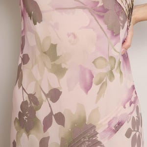 K&ouml;nnte beinhalten: Ein rosa- und lilafarbenes Kleid mit floralem Druck und einem diagonalen Faltendetail. Das Kleid hat kurze &Auml;rmel und einen flie&szlig;enden Rock.