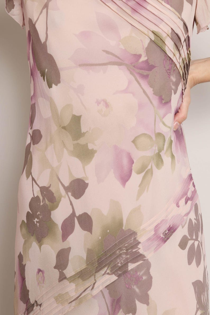 K&ouml;nnte beinhalten: Ein rosa- und lilafarbenes Kleid mit floralem Druck und einem diagonalen Faltendetail. Das Kleid hat kurze &Auml;rmel und einen flie&szlig;enden Rock.