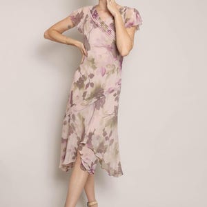 K&ouml;nnte beinhalten: Ein rosafarbenes und violettes Midi-Kleid mit Blumenmuster, V-Ausschnitt und kurzen &Auml;rmeln. Das Kleid hat eine flie&szlig;ende Silhouette und einen R&uuml;schen-Saum.