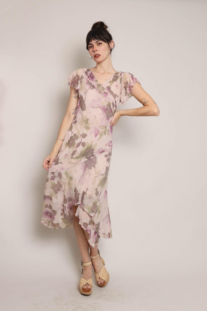 K&ouml;nnte beinhalten: Ein rosafarbenes Midi-Kleid mit floralem Druck, V-Ausschnitt und kurzen &Auml;rmeln. Das Kleid hat einen R&uuml;schen-Saum und eine High-Low-Silhouette.