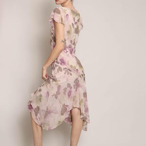 K&ouml;nnte beinhalten: Ein rosafarbenes und violettes Midi-Kleid mit floralem Muster, R&uuml;schen am Ausschnitt und kurzen &Auml;rmeln. Das Kleid hat einen flie&szlig;enden, asymmetrischen Saum.