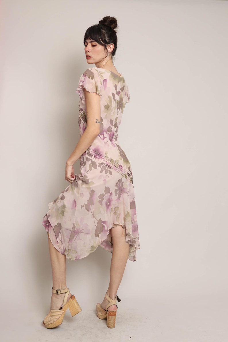 K&ouml;nnte beinhalten: Ein rosafarbenes und violettes Midi-Kleid mit floralem Muster, R&uuml;schen am Ausschnitt und kurzen &Auml;rmeln. Das Kleid hat einen flie&szlig;enden, asymmetrischen Saum.